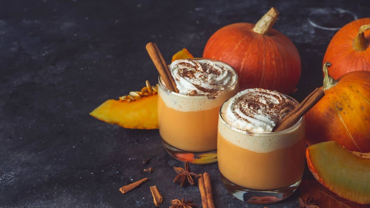 Deux verres de latte à la citrouille à côté de quelques citrouilles.