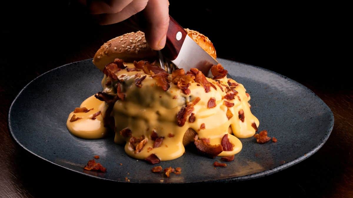 Découpe d'un hamburger chargé de fromage fondu et de bacon.