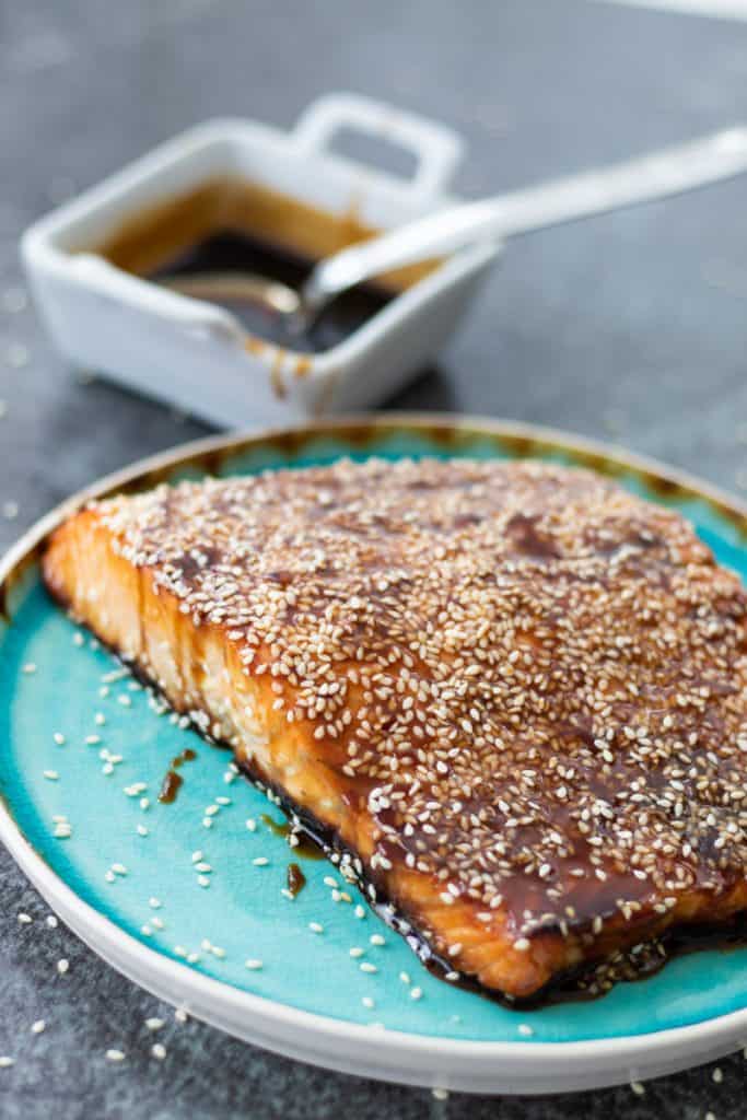 vue latérale du saumon teriyaki nappé de sauce teriyaki et servi sur une assiette turquoise, avec un bol de sauce teriyaki en arrière-plan