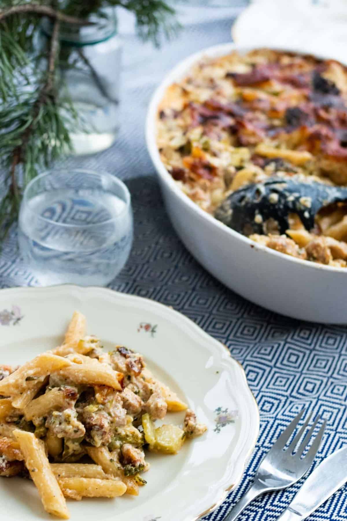 une assiette de gratin de pâtes au poulet et brocoli devant un verre d'eau et une casserole pleine de gratin de pâtes