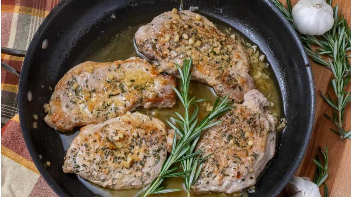 Côtelettes de porc à l'ail et au parmesan avec des brins de romarin dans une poêle noire.