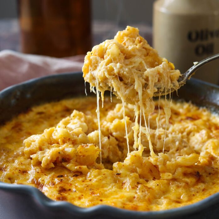 A spoonful of gouda mac and cheese being lifted out of the pan with a cheese pull.