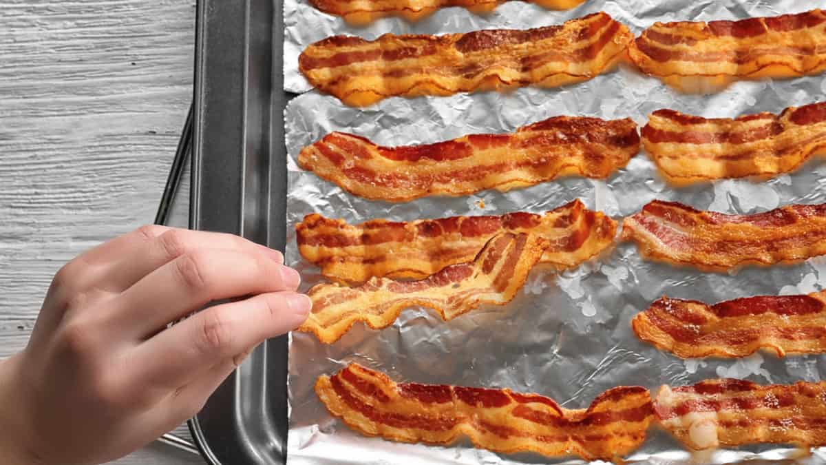 Bacon croustillant cuit sur une plaque de cuisson, avec une main prenant un morceau.