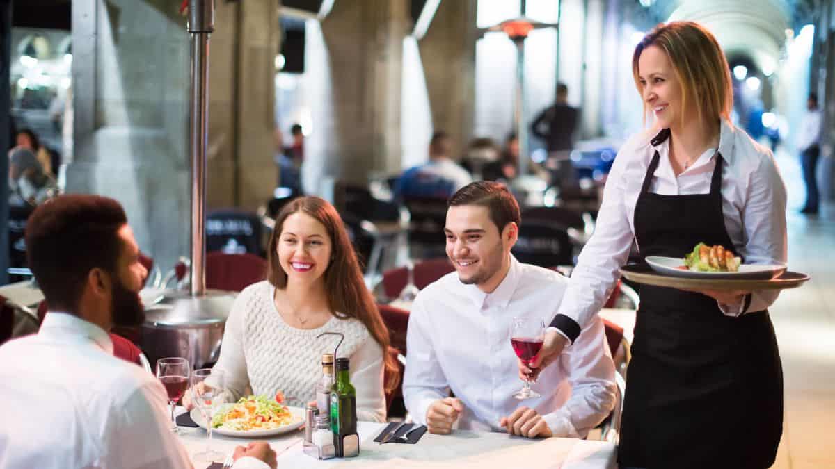 Trois personnes à une table servies par une femme.