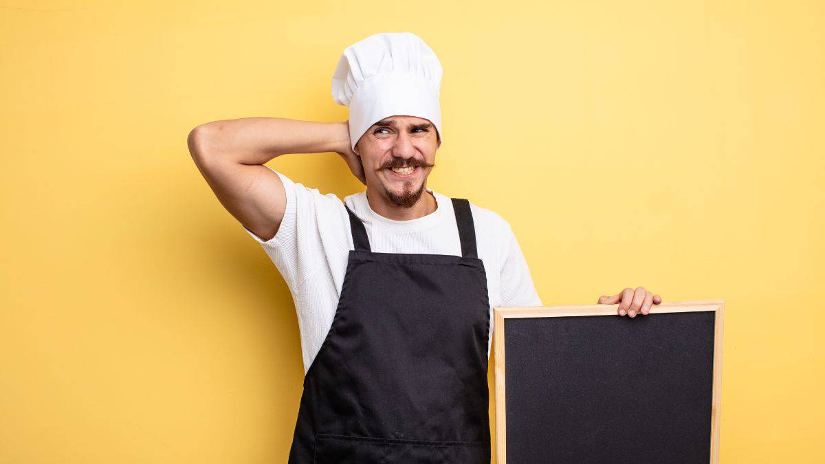 Un homme avec un chapeau de chef et un tableau noir.