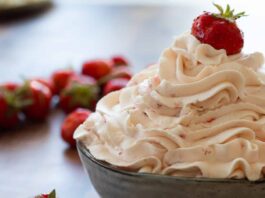 Crème Fouettée aux Fraises : Astuces et Recettes Incontournables strawberry whipped cream in a bowl topped with a strawberry.